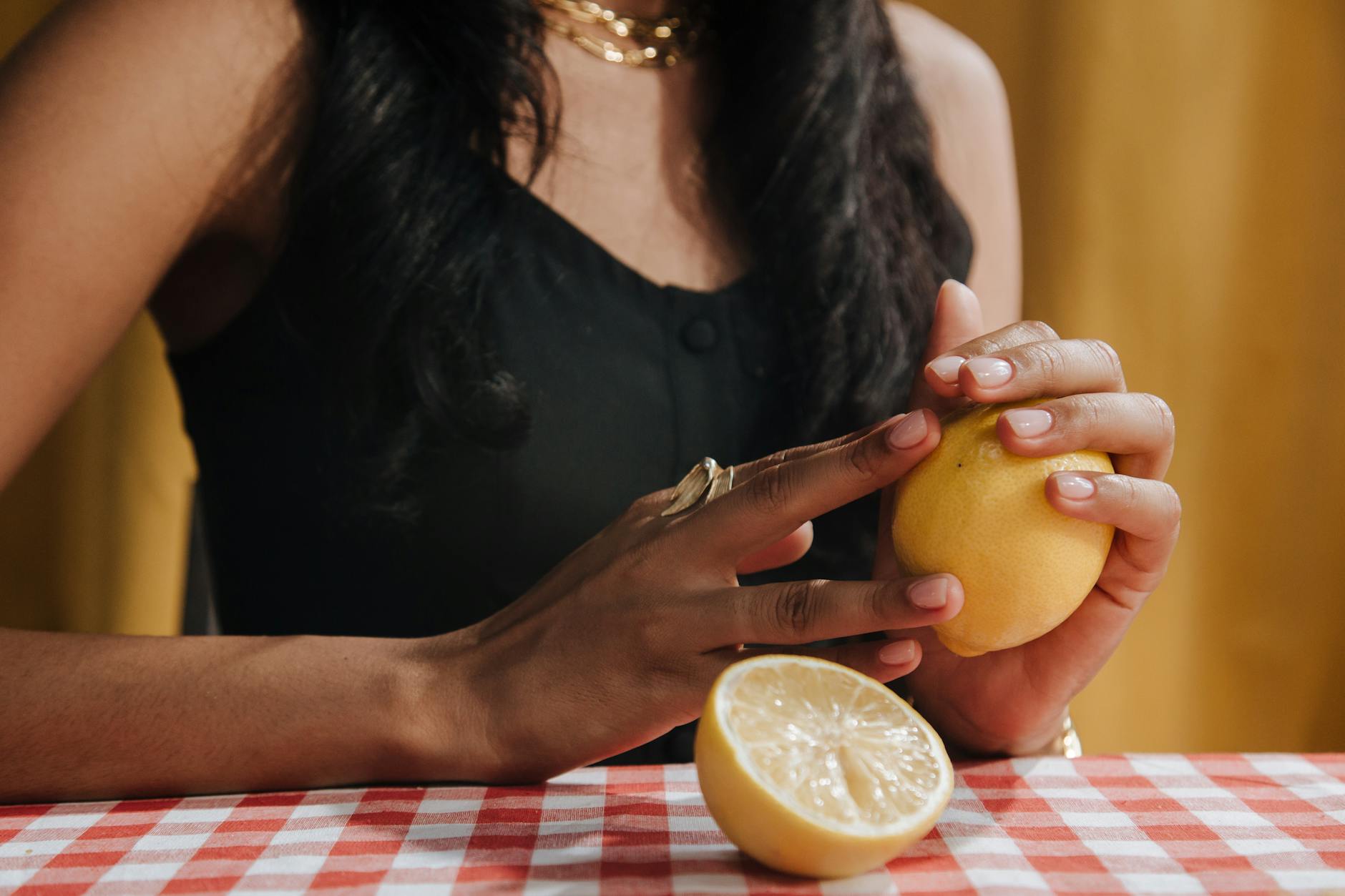 A hand holding a fresh lemon on a soft pink background, representing the lemon vibrator's shape and gentle approach.