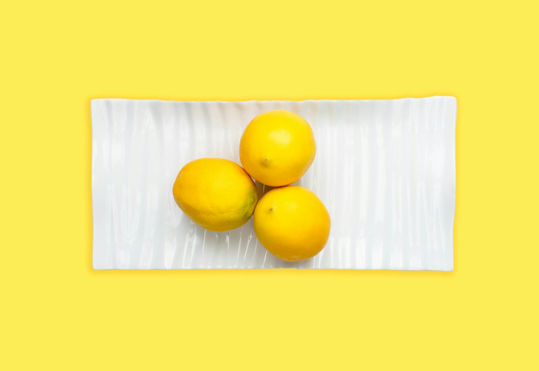 Fresh lemons arranged on a white plate with a vibrant yellow background