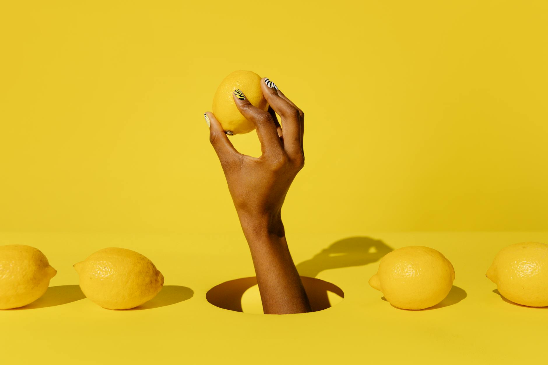 A hand holding a fresh lemon on a vivid yellow background