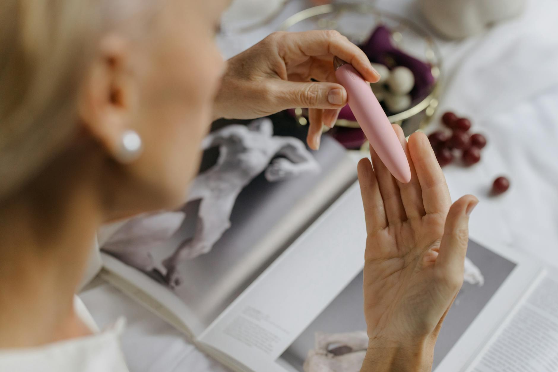 Close-up of a woman with intimate wellness products surrounded by art books on a personal shelf