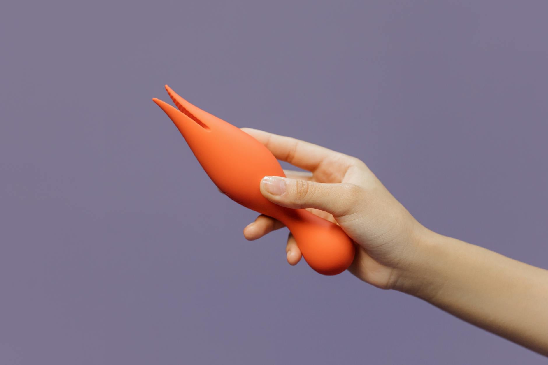 A hand holding a lemon-colored clitoral vibrator against a minimalist purple backdrop