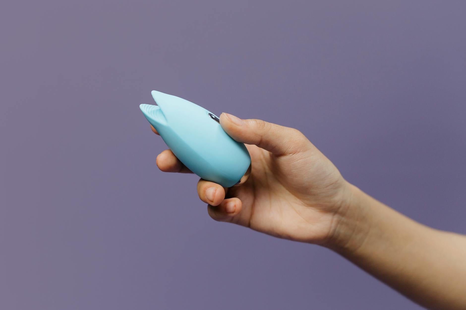A sleek teal lemon clitoral vibrator on smooth white silk fabric